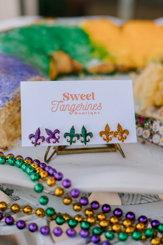 Card with colorful earrings on a stand, surrounded by Mardi Gras beads and a blurred background.