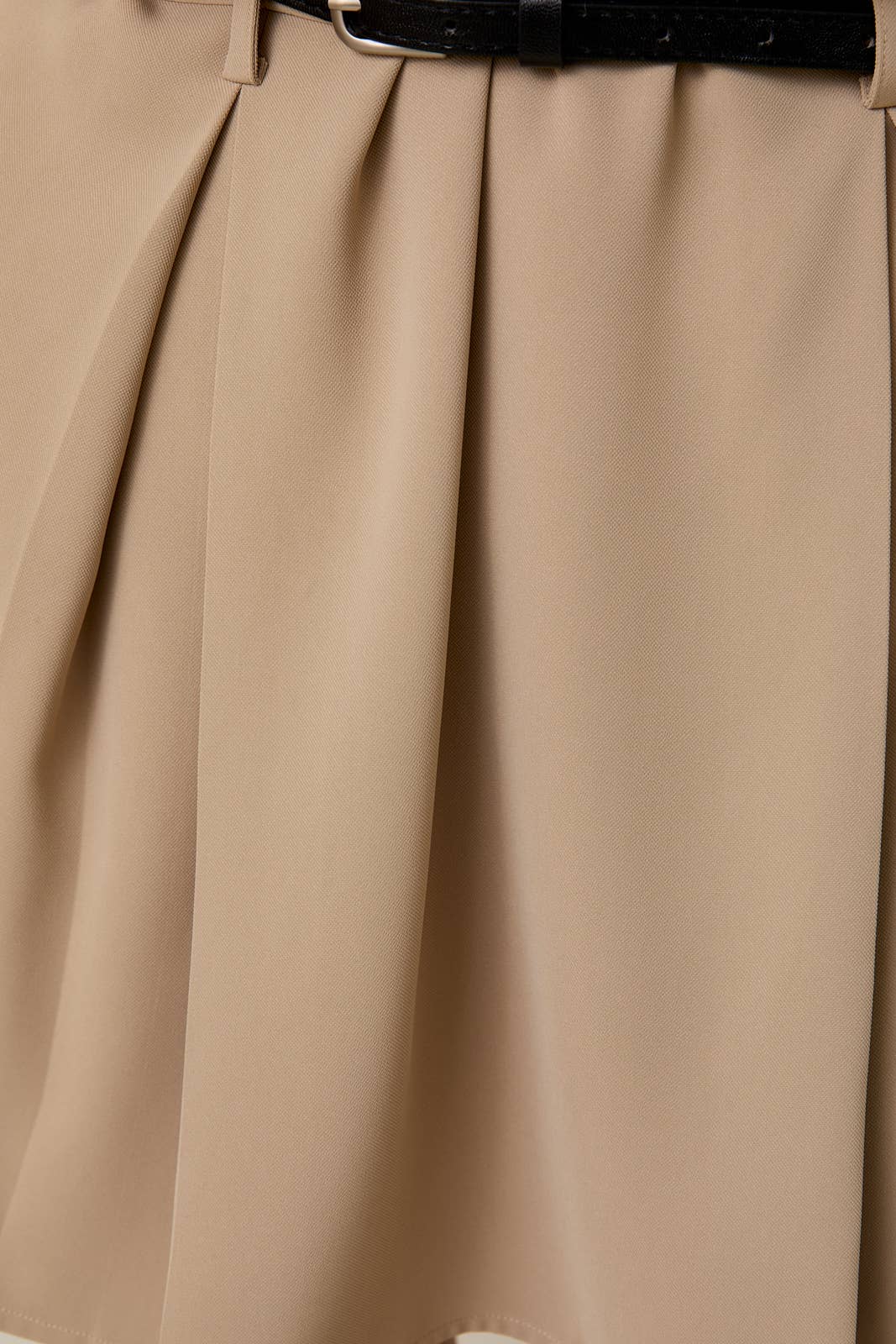 Close-up of beige pleated skirt with a black belt.