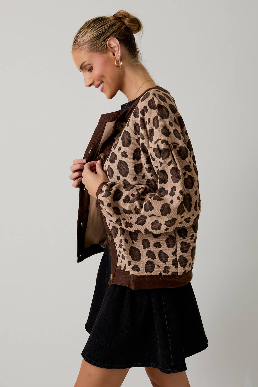 Woman wearing a leopard print sweater over a black dress against a plain background