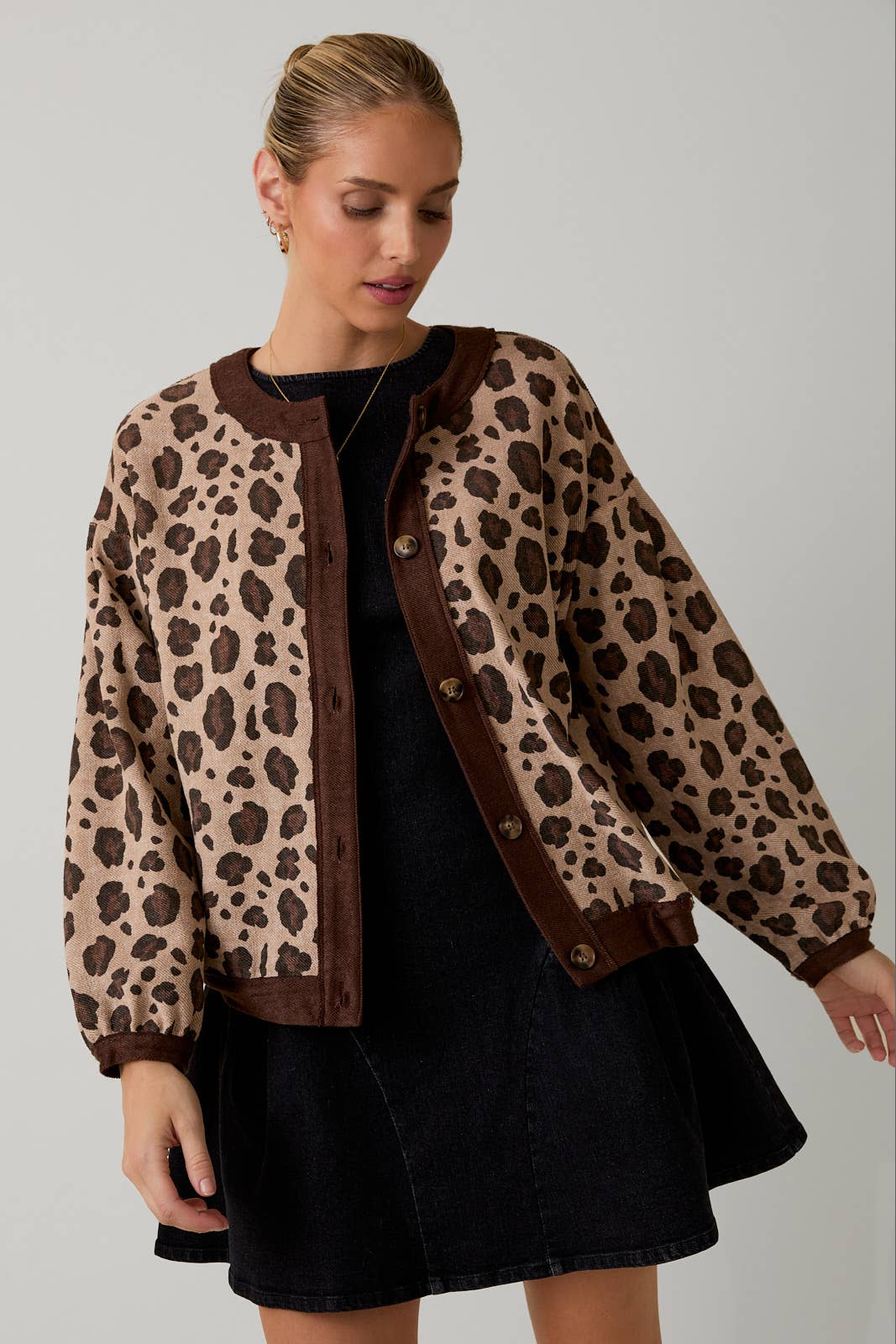 Woman wearing a leopard print cardigan over a black dress on a gray background