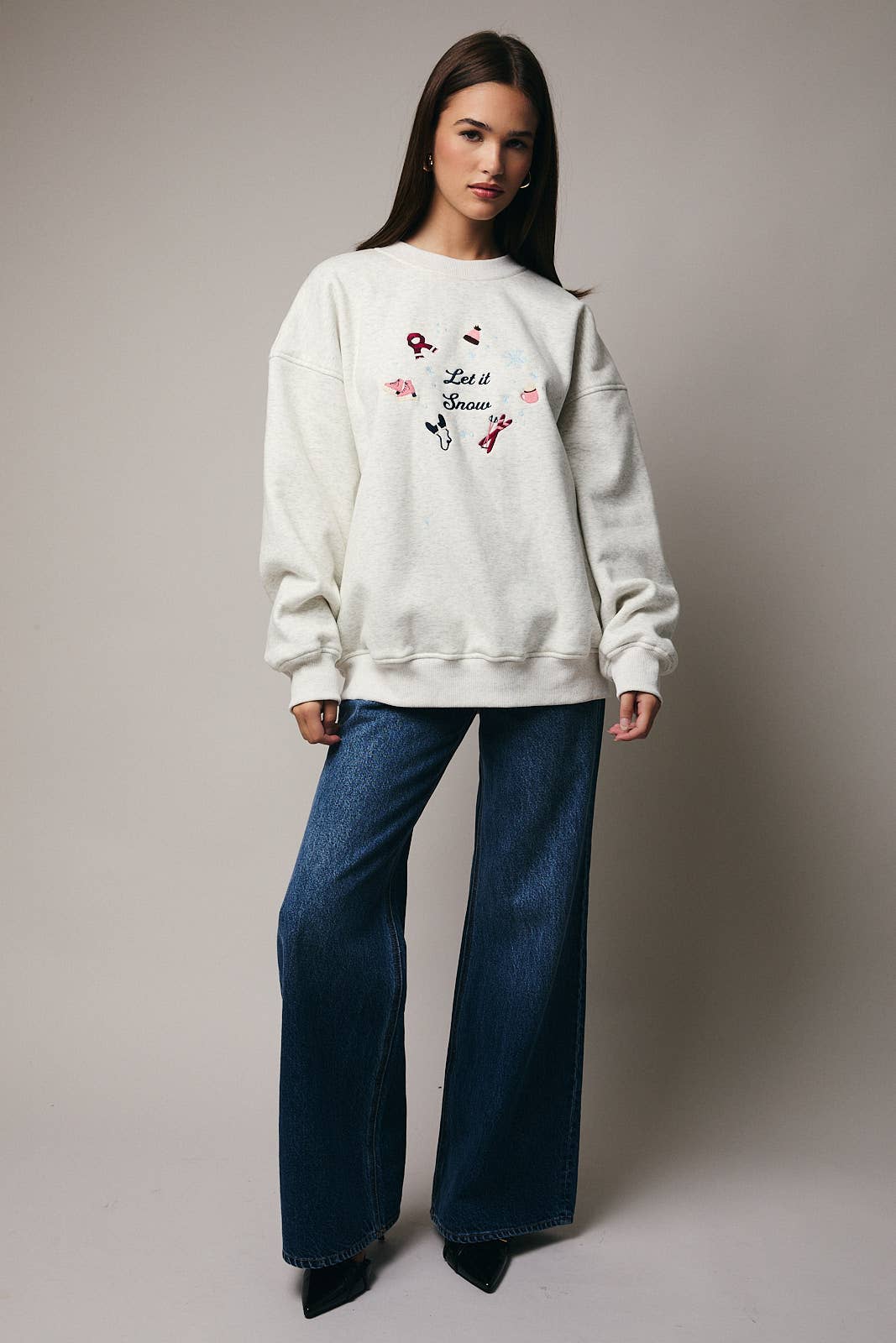Woman wearing a white sweatshirt with graphics and text, paired with blue jeans on a plain background