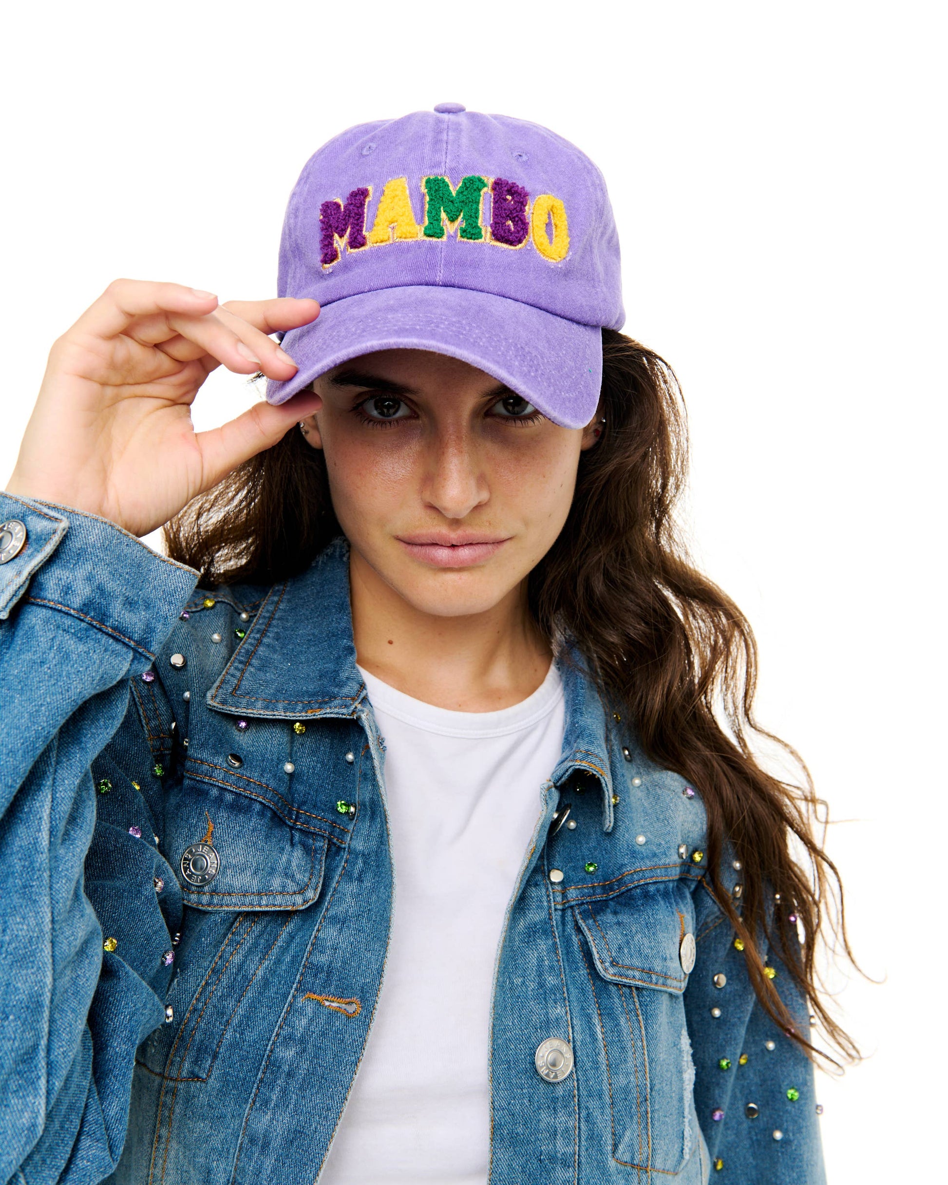 Person wearing a purple cap with 'MAMBO' in colorful letters, holding it with one hand.