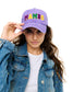 Person wearing a purple cap with 'MAMBO' in colorful letters, holding it with one hand.