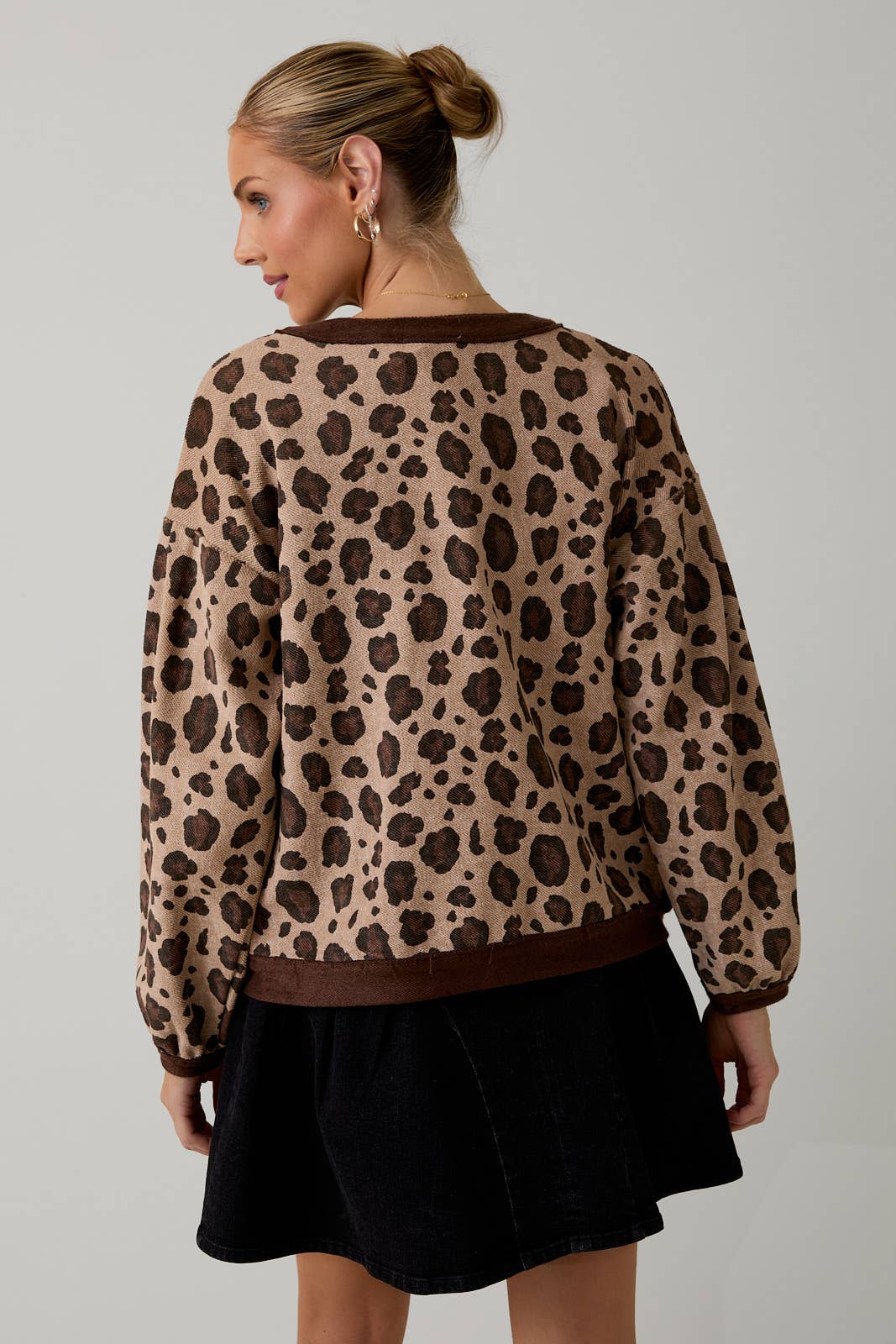 Person wearing a leopard print sweater and black skirt on a plain background
