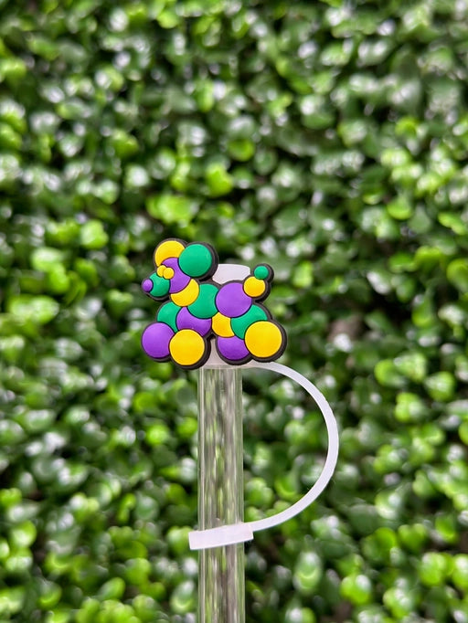 A multicolored silicone straw topper fitted on a straw, with a blurred greenery background.