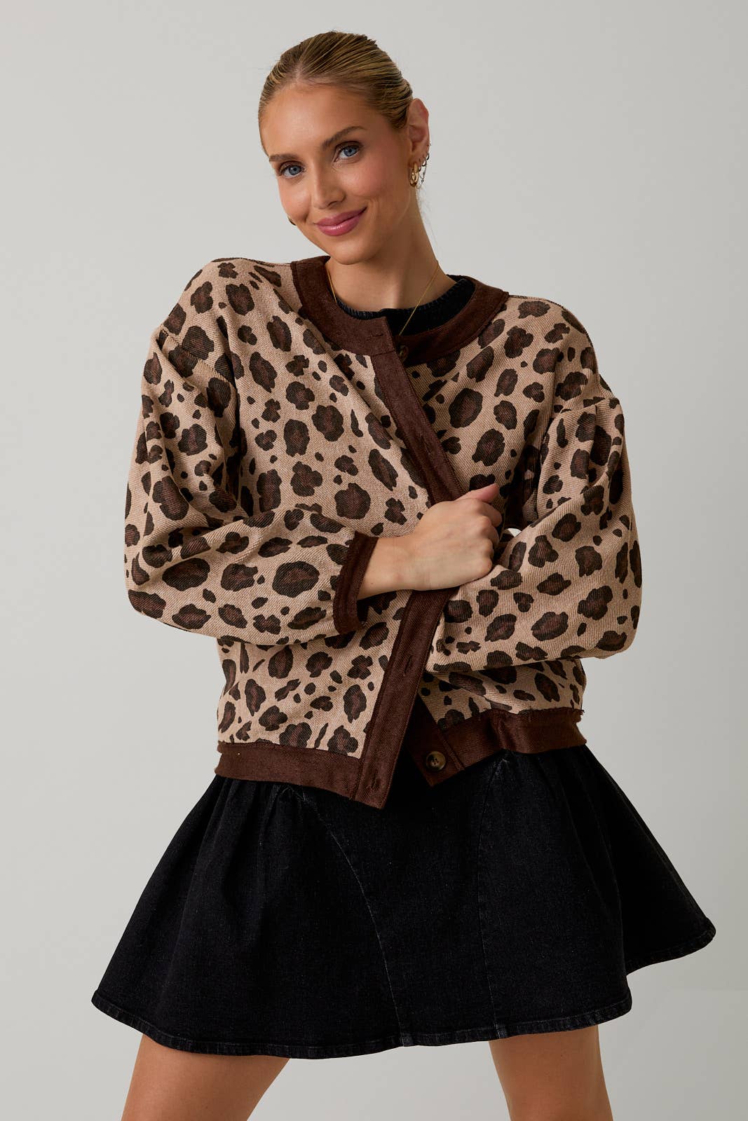 Woman wearing a leopard print cardigan over a black top and skirt on a plain background