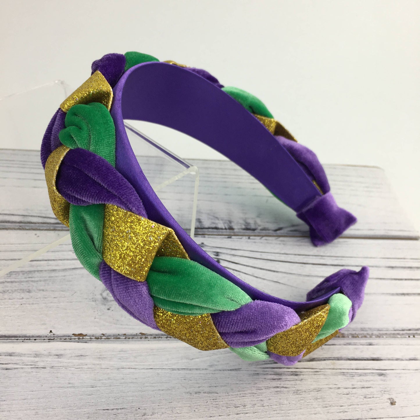 Purple, green, and gold braided headband on a wooden surface