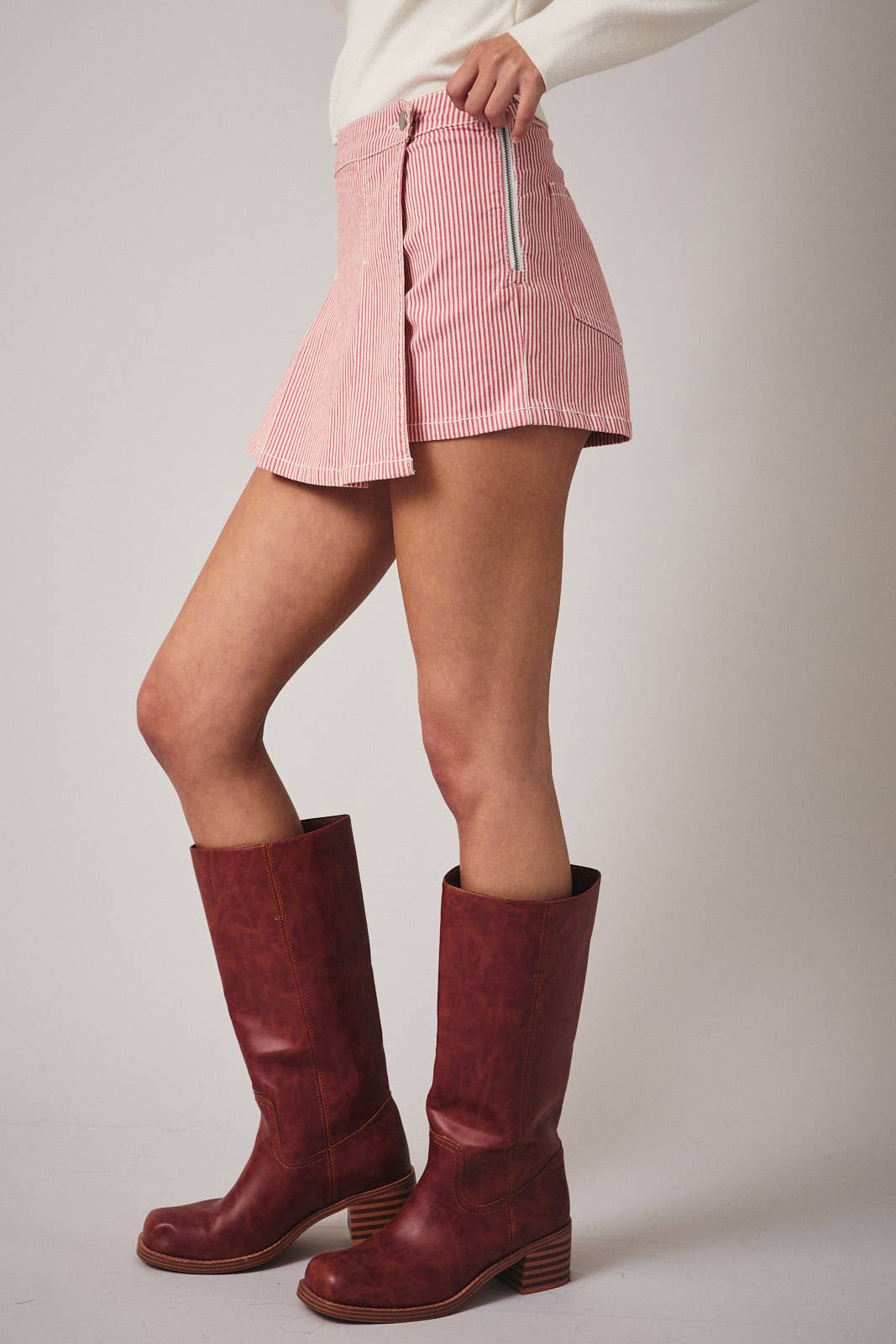 Person wearing a pink skirt and red boots on a plain background
