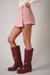 Person wearing a pink skirt and red boots on a plain background