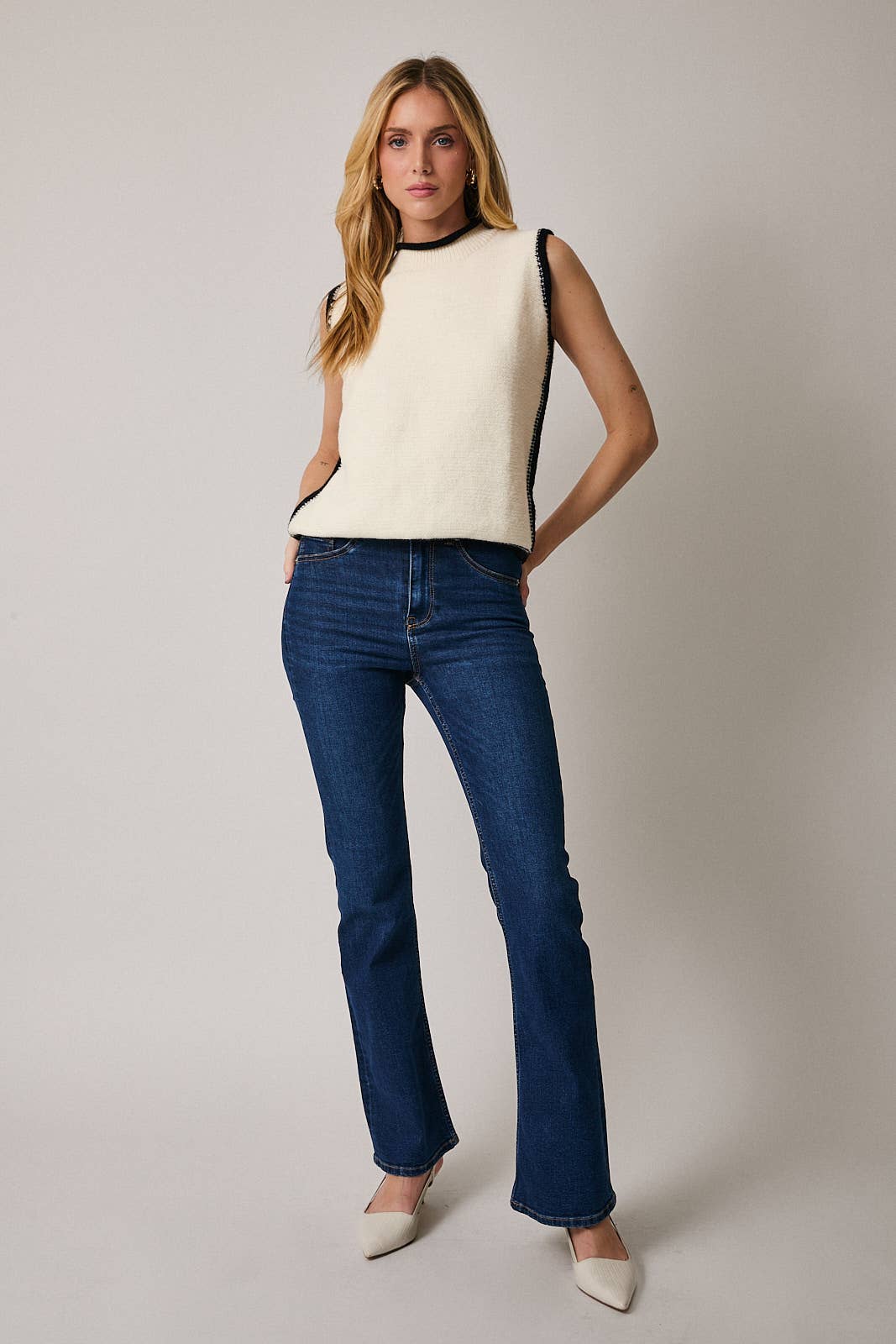 Woman wearing a white sleeveless top and blue jeans against a plain background