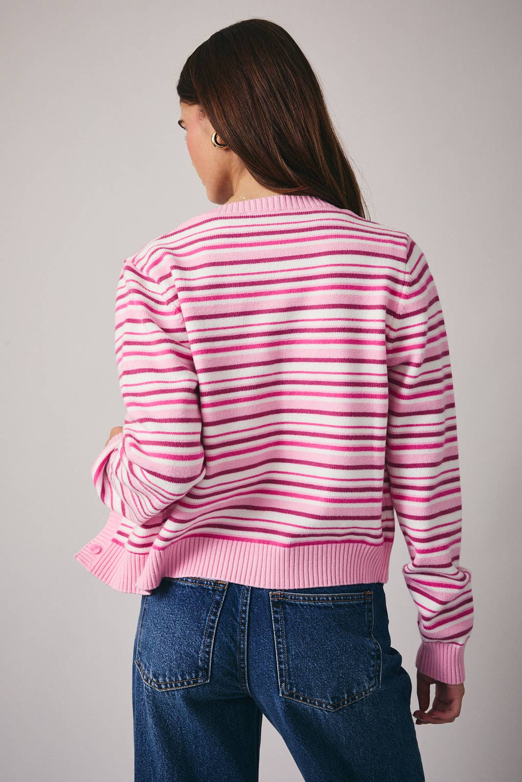 Person wearing a pink and white striped sweater and blue jeans on a gray background