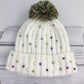 White knit beanie with colorful beads and a pom-pom on a wooden surface