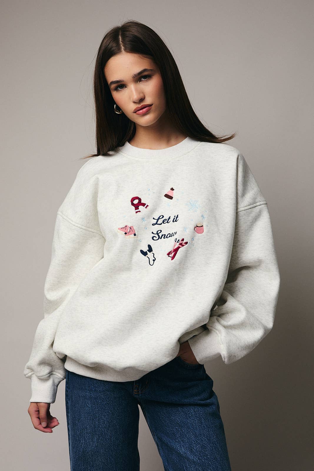 Woman wearing a white sweatshirt with a snow-themed design on a plain background