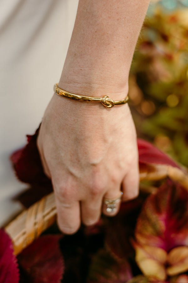 Close-up of a hand wearing a gold bracelet with a blurred background