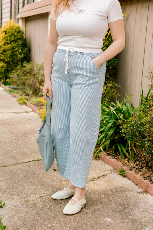 Person wearing light blue striped pants and a white top, standing outdoors.