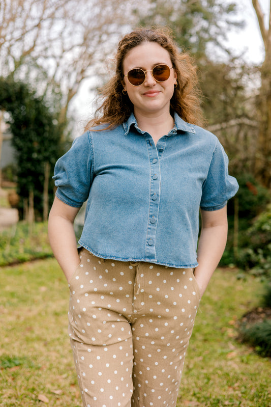 Woman wearing a blue denim shirt and beige polka dot pants standing outdoors.