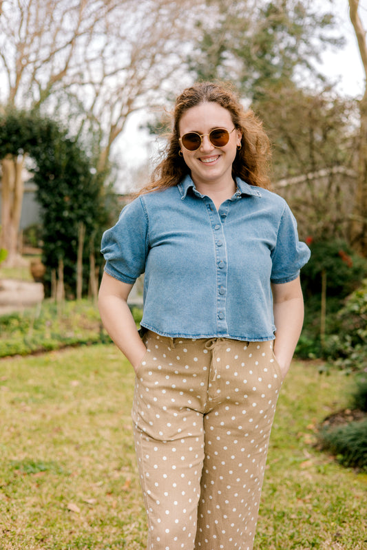 Woman wearing a blue denim shirt and beige polka dot pants standing outdoors.