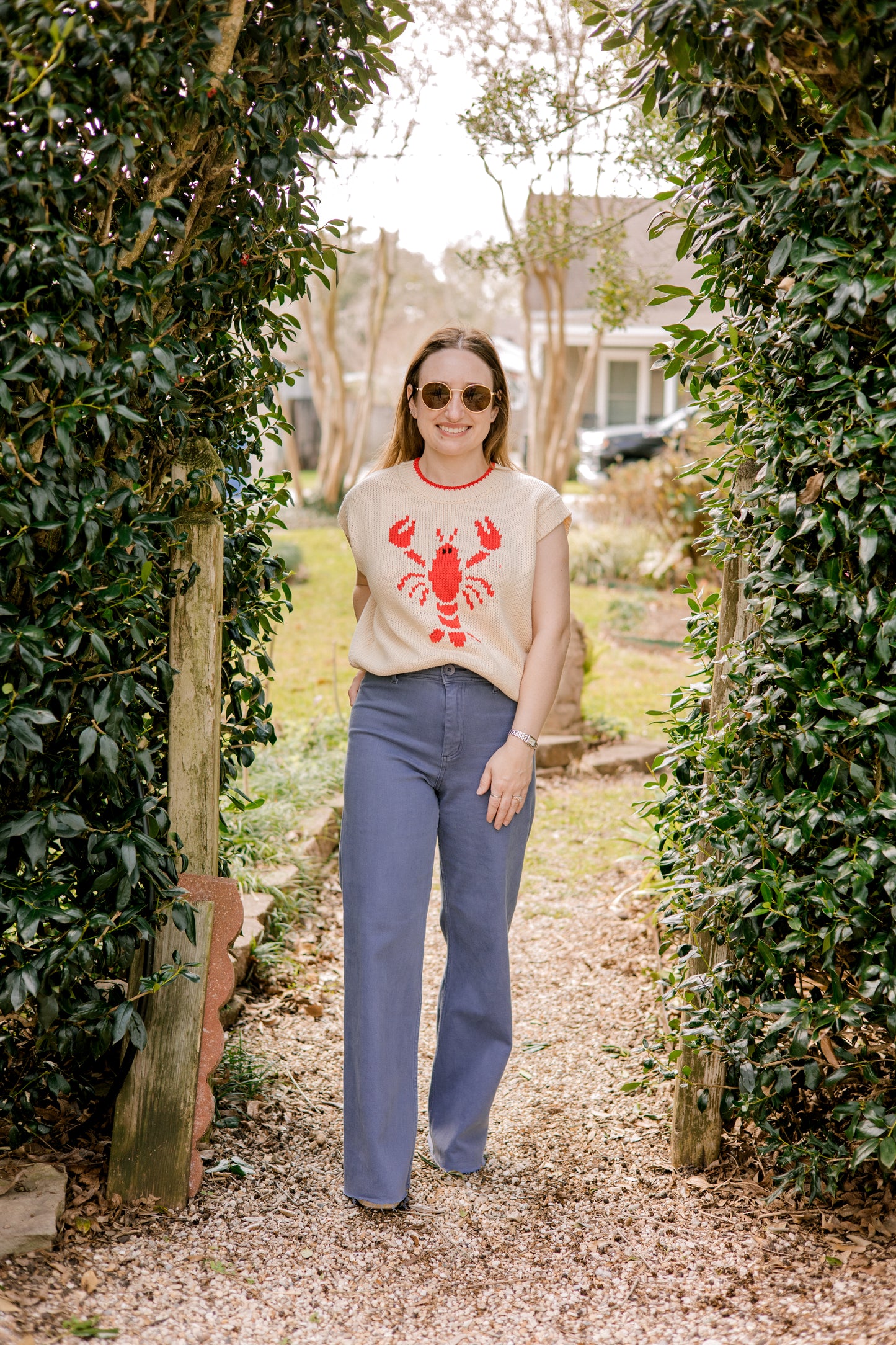Woman walking through a garden wearing a sweater with a lobster design.
