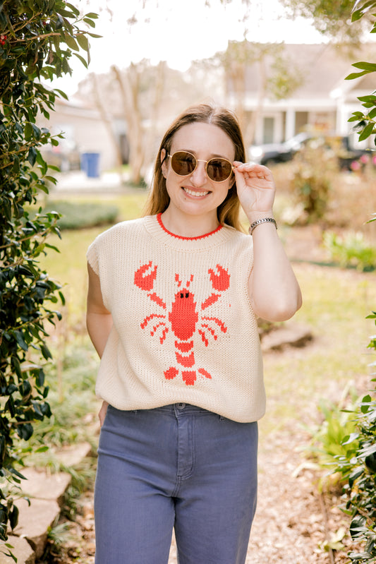 Woman wearing a sleeveless sweater with a lobster design outdoors.