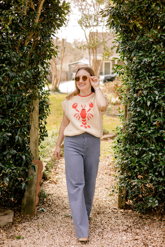 Woman wearing a sweater with a red lobster design, walking through a garden path.