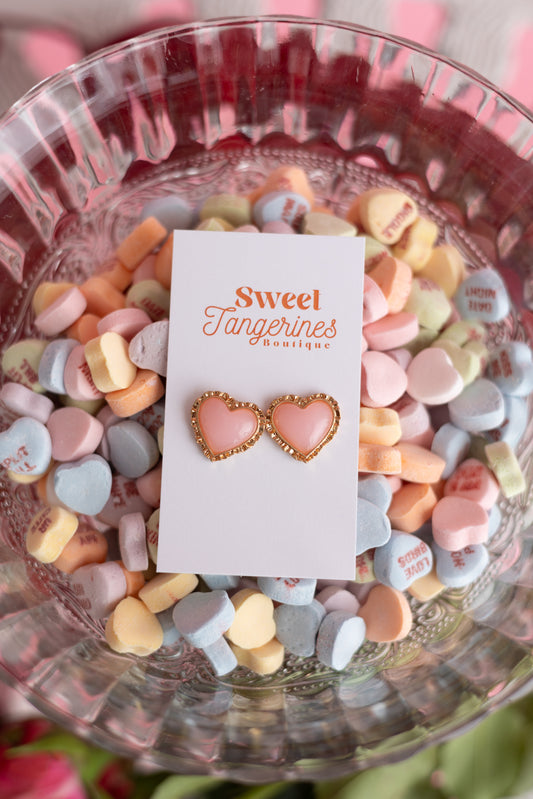 Heart-shaped earrings on a card with 'Sweet Tangerines Boutique' text, surrounded by colorful candy hearts in a glass bowl.
