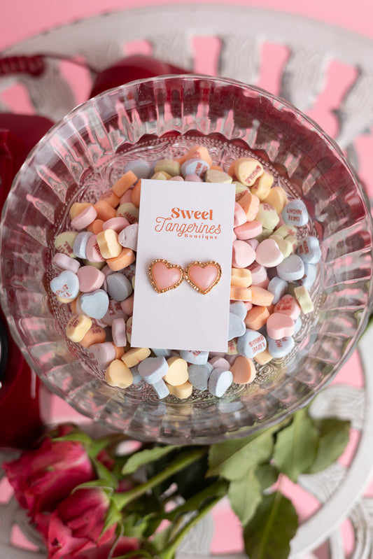 Heart-shaped earrings on a card with 'Sweet Tangerines' branding, surrounded by colorful candy in a glass bowl.