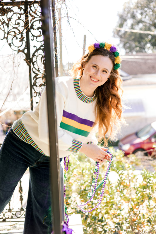 Woman wearing a colorful striped sweater and Mardi Gras beads outdoors.