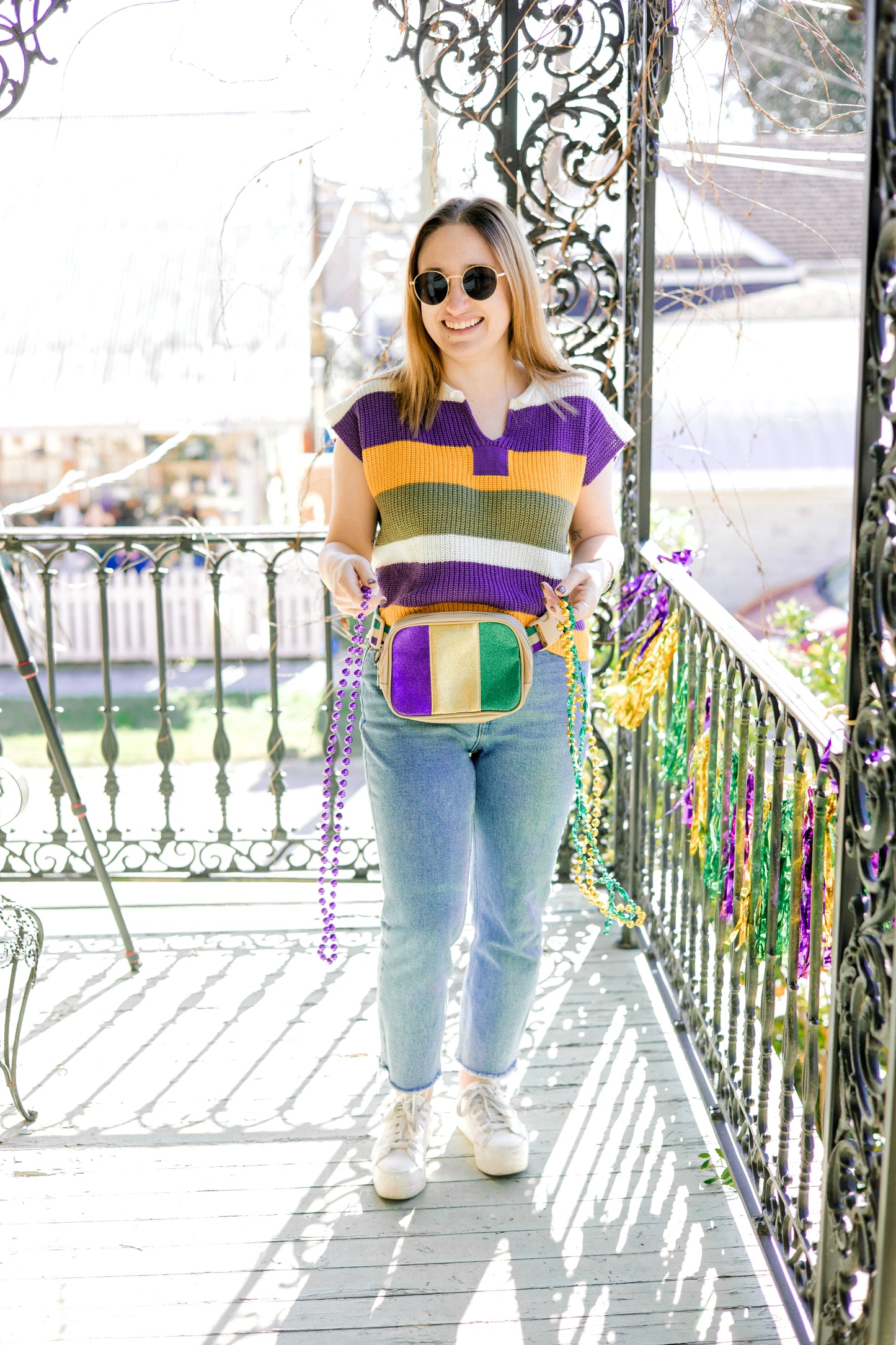 Woman wearing a colorful striped shirt and jeans on a balcony with Mardi Gras beads.