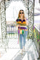 Woman on a porch with Mardi Gras decorations, wearing sunglasses and a colorful striped shirt.