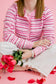 Person wearing a pink striped sweater holding red roses on a pink background