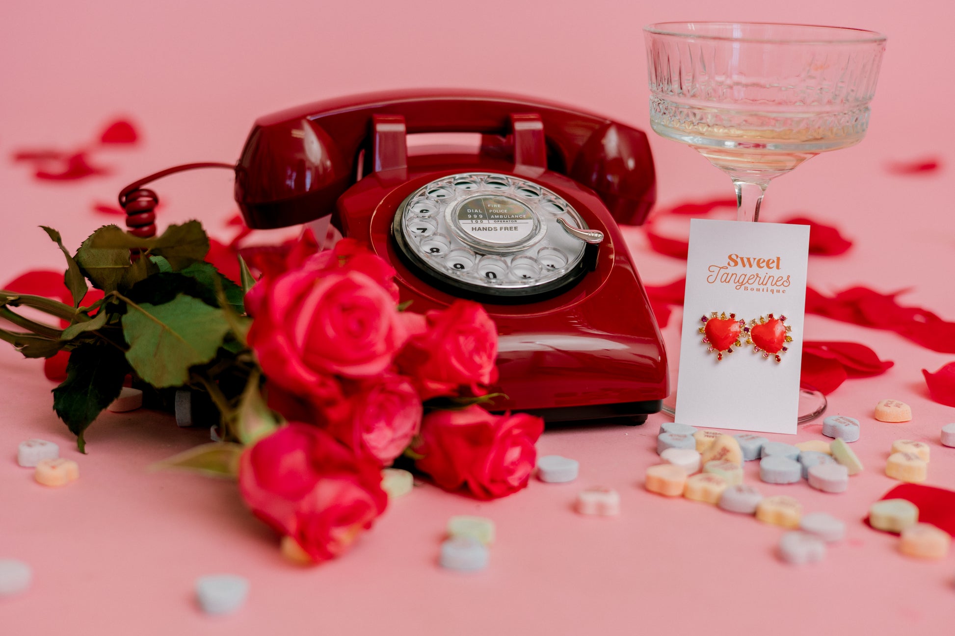 Vintage red rotary phone with roses, candy, and a glass on a pink background