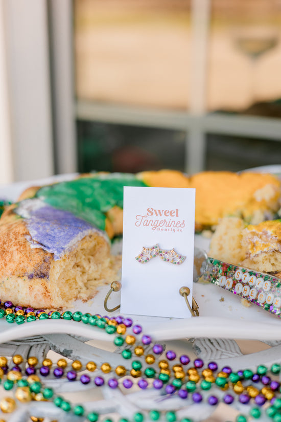 Earrings on a card with Mardi Gras beads and pastries in the background