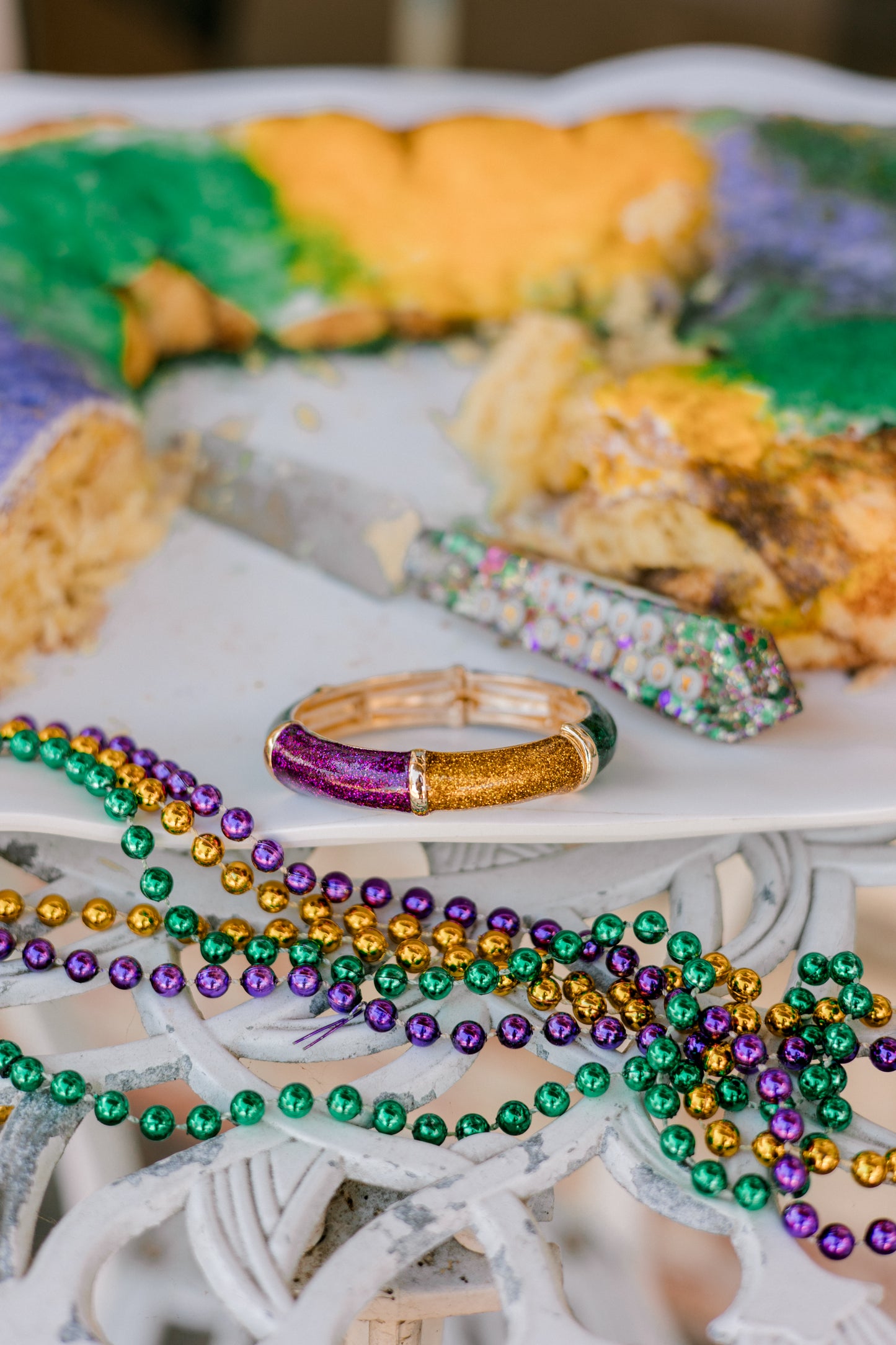 Mardi Gras beads and a bangle on a decorative cake with colorful icing.