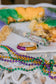 Mardi Gras beads and a bangle on a decorative cake with colorful icing.