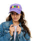 Person wearing a purple cap with 'MAMBO' in colorful letters, denim jacket with sequins, and white shirt.
