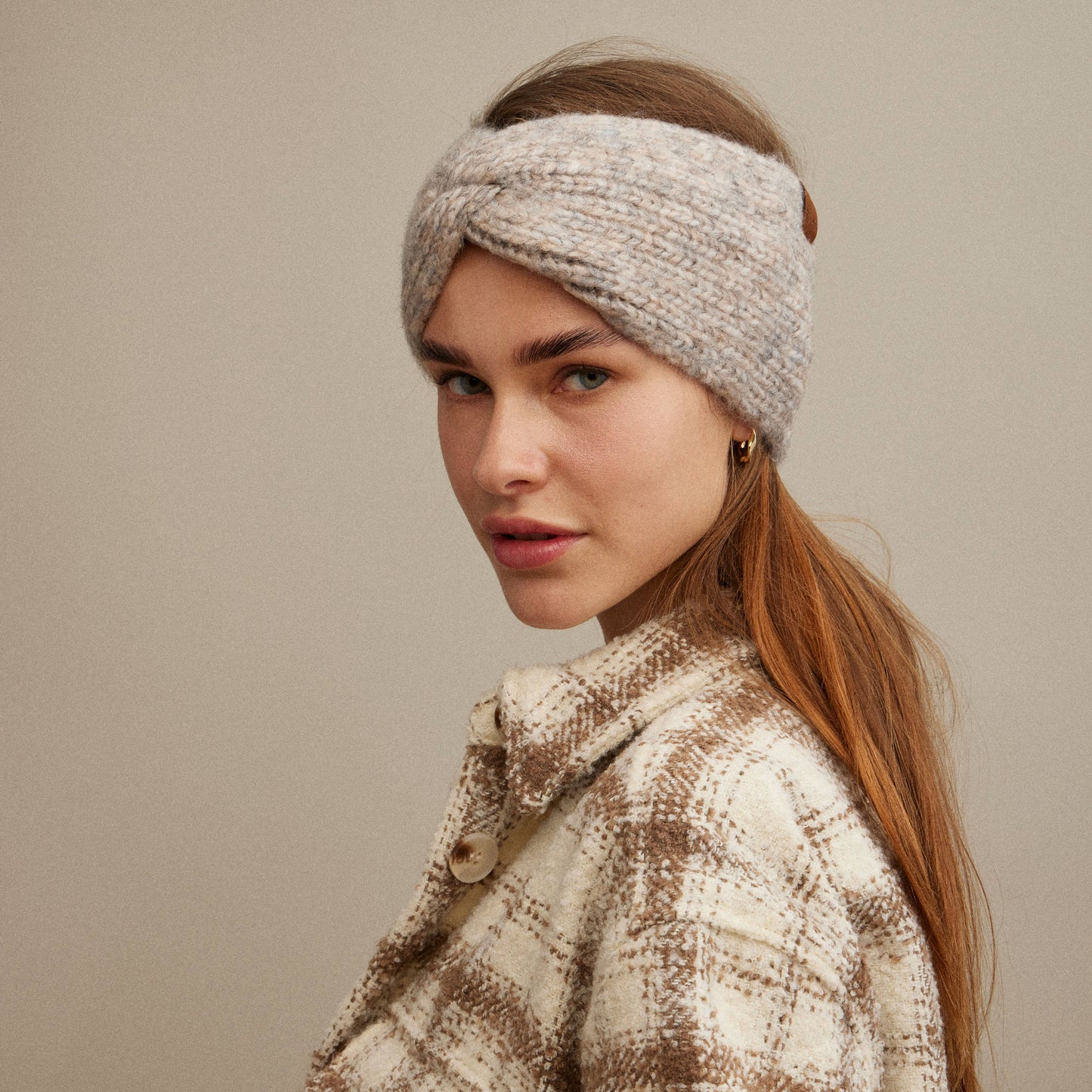 Woman wearing a knitted headband and plaid coat against a neutral background