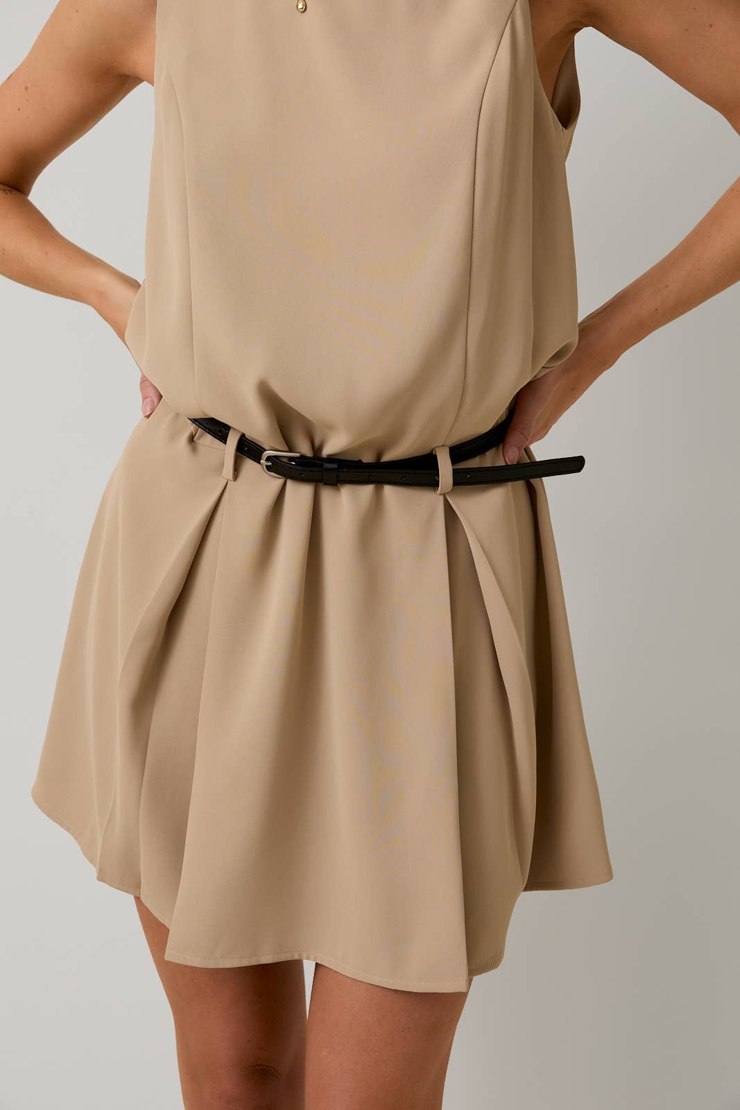 Beige dress with a black belt on a plain background