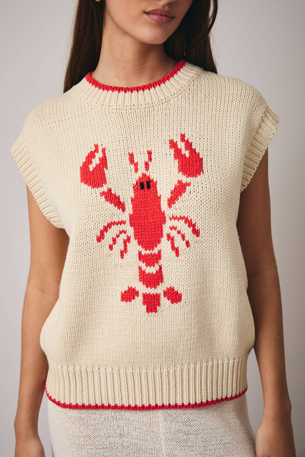 Beige sweater with red lobster design worn by a person on a neutral background