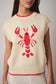 Beige sweater with red lobster design worn by a person on a neutral background