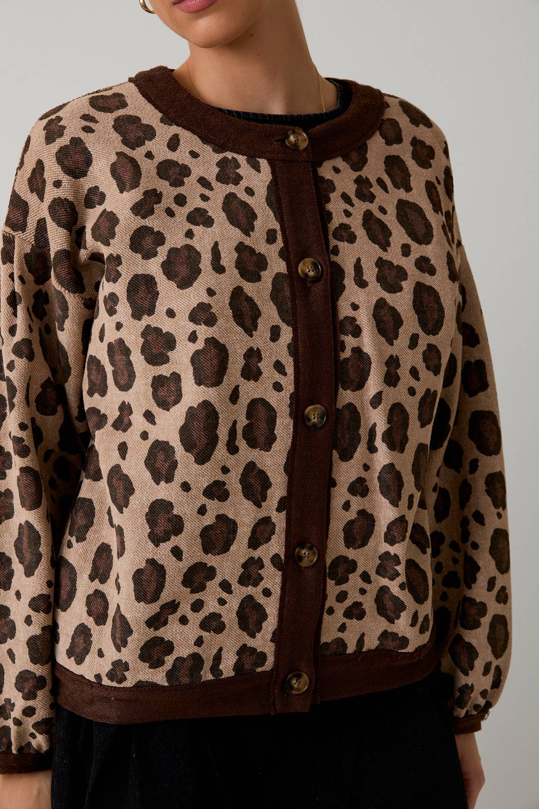 Leopard print cardigan with brown trim on a neutral background