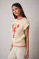 Woman wearing a cream sweater with red accents and a lobster design on a plain background