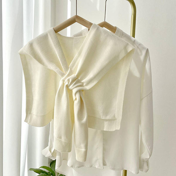 Cream-colored cardigan on a wooden hanger against a white curtain background