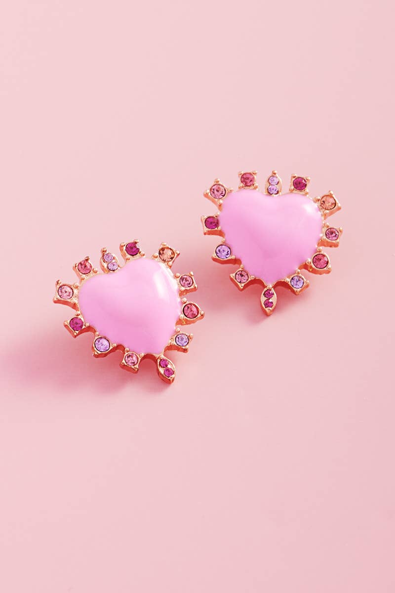 Heart-shaped pink earrings with gemstone accents on a pink background