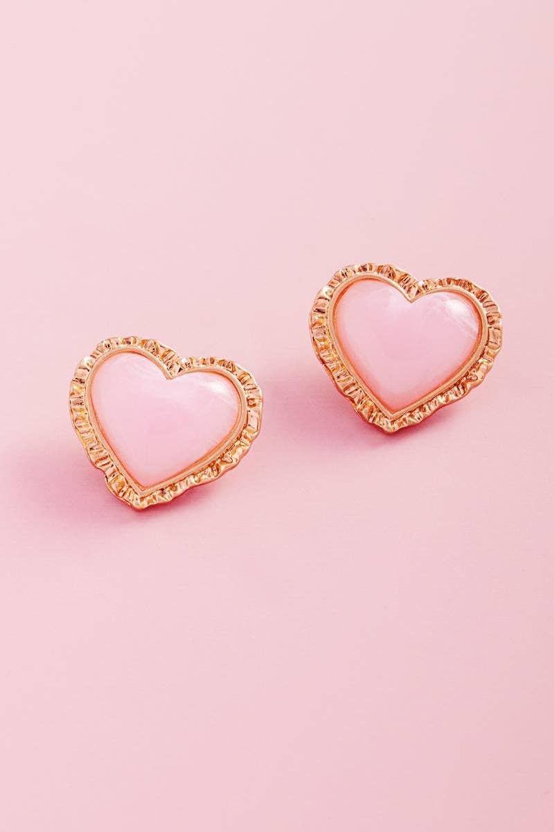 Heart-shaped earrings with gold frames and pink centers on a pink background