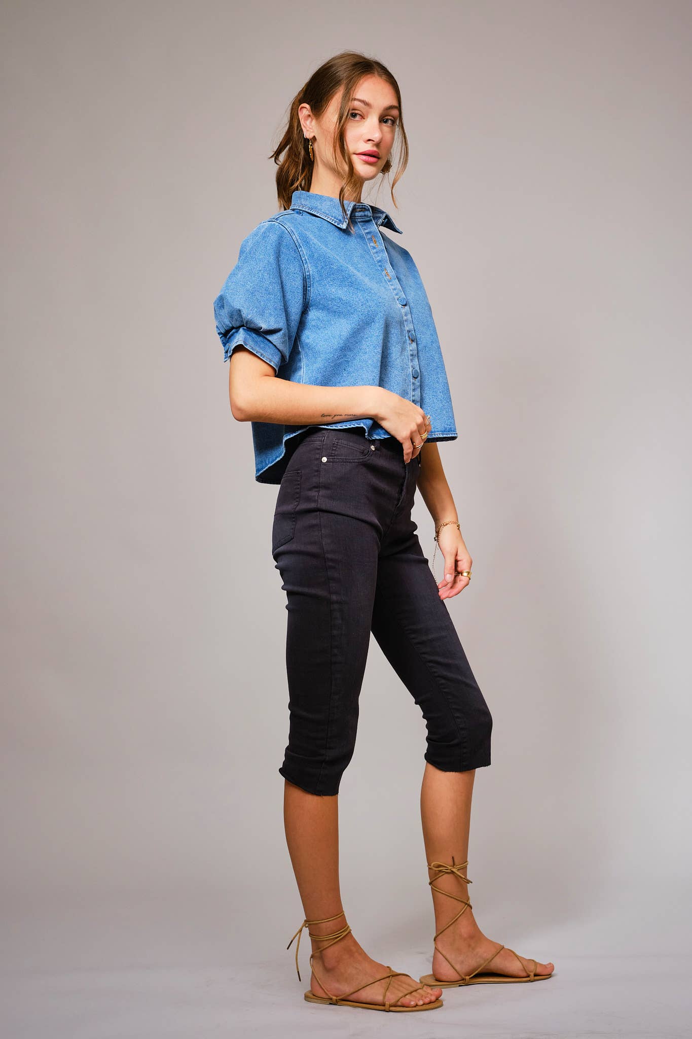 Woman wearing a blue denim shirt and black pants against a gray background